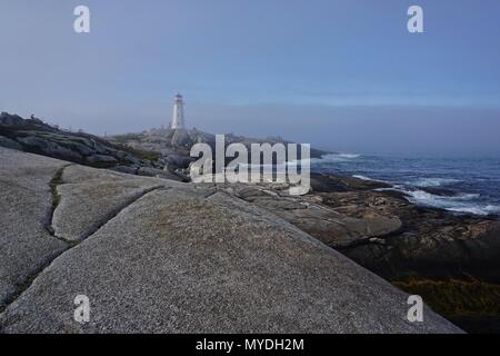 Peggy's Cove, Nova Scotia, Canada: Peggy's Point Lighthouse (1914) è avvolta nella nebbia di mattina con le onde che si infrangono sulla costa rocciosa. Foto Stock