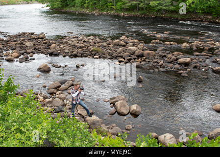 Un fotografo in piedi sulle rocce sul bordo del fiume Hudson vicino al fiume del Nord, NY USA nelle Montagne Adirondack Foto Stock