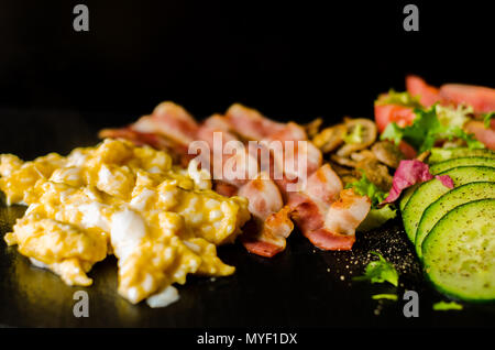 Uova strapazzate con bacon, funghi porcini servito con insalata di pomodori e cetrioli, set colazione Foto Stock