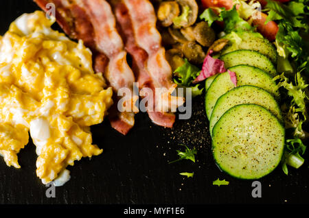 Uova strapazzate con bacon, funghi porcini servito con insalata di pomodori e cetrioli, set colazione Foto Stock