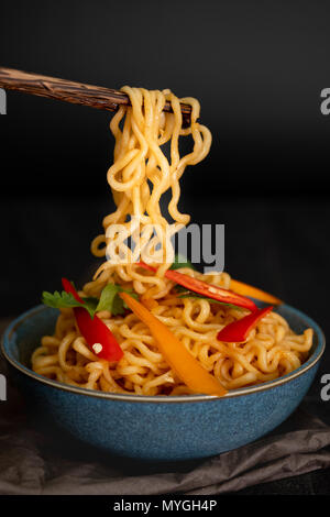 Ancora vita spaghetti istantanei con fette di peperone su chopstick, cibo spazzatura o fast food concept. Foto Stock