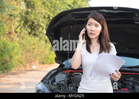 Asia giovane donna seduta di fronte la sua automobile, provare a chiamare per ricevere assistenza con la sua vettura rotto verso il basso Foto Stock