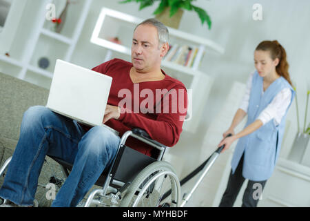 Disabilitato l uomo di casa utilizzando laptopwoman la pulizia in background Foto Stock