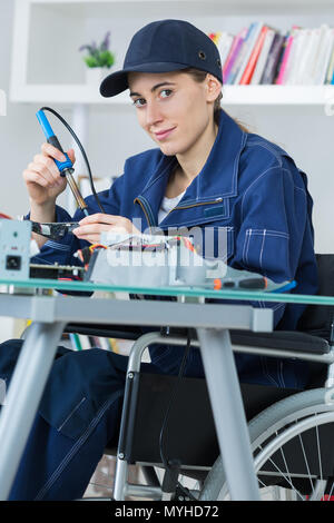 Tecnico femminile su una sedia a rotelle la saldatura di un circuito elettronico Foto Stock
