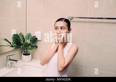 Donna felice deterge la pelle con la schiuma in bagno. Foto Stock