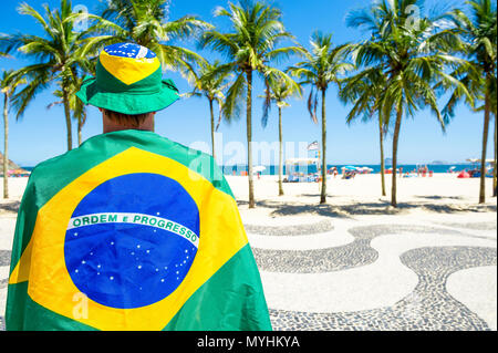 Orgoglioso brasiliano in bandiera regalia in piedi di fronte a Copacabana Beach skyline della città di Rio de Janeiro in Brasile Foto Stock