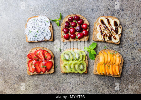 Tradizionale americana ed europea e in estate la colazione: sandwich di pane tostato con burro di arachidi, di bacche e frutti pesca, fragola, banana, ciliegia, kiwi Foto Stock