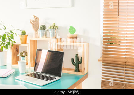 Finestra con persiane in legno nella sala bianca interno con home office desk con laptop, tazza di caffè, con un decor fresco e cactus Foto Stock