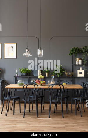 Sedie nere al tavolo di legno in grigio sala da pranzo interno con lampade e piante. Foto reale Foto Stock