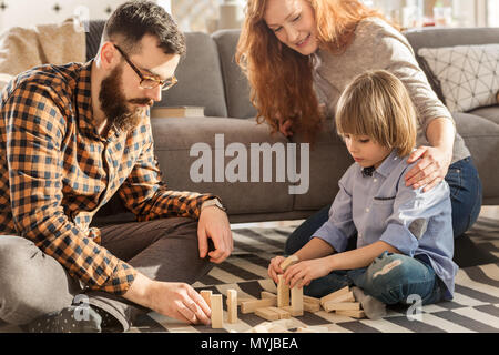 I giovani genitori a giocare con il loro bambino con blocchi di legno in soggiorno spazioso Foto Stock