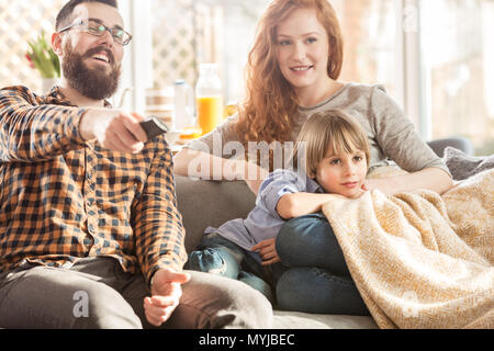 La famiglia felice guardando la TV insieme sul divano nel soggiorno moderno Foto Stock