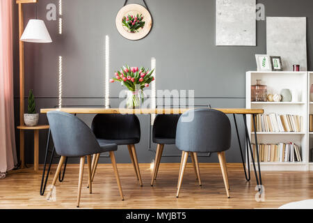 Tavolo da pranzo in legno, sedie grigio, scaffale e tulipani rosa in sala da pranzo interno Foto Stock