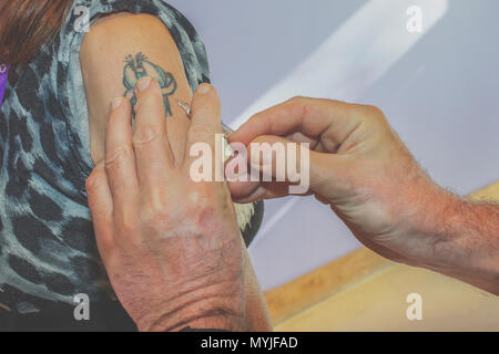 Medico dà una iniezione intramuscolare in braccio femmina con tattoo Foto Stock
