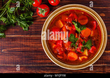 Gulasch o stufato di carne nella terrina servita con prezzemolo su sfondo di legno, vista dall'alto. Foto Stock