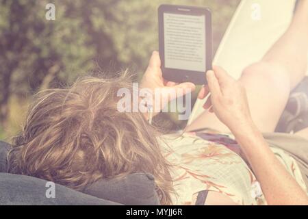 Donna sdraiata sulla sedia a sdraio di lettura di un ebook sotto il sole Foto Stock