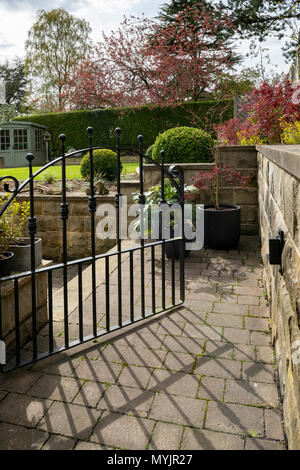 Vista attraverso il cancello aperto al bello, paesaggistico giardino privato con un design contemporaneo, arbusti, box sfere, percorso e ordinato prato - Yorkshire, Inghilterra, Regno Unito Foto Stock