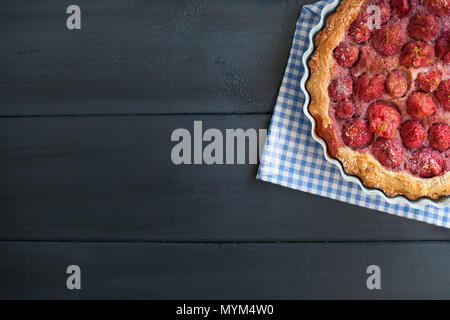 Aprire la torta con le fragole in vaso blu per la prima colazione, su un nero lo sfondo di legno. In casa la cottura. Spazio libero per il testo. Spazio di copia . Lay piatto. Foto Stock