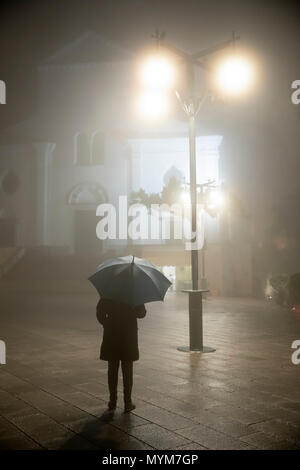 Persona con ombrellone in piedi sotto il lampione di fronte al duomo di pioggia e nebbia di notte, Ravello, la Costiera Amalfitana, Campania, Italia, Europa Foto Stock