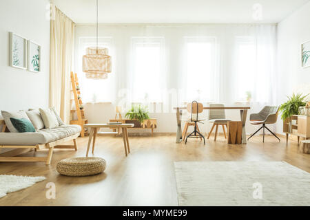 Pouf accanto al divano beige con cuscini in salotto luminoso interno con tavoli e sedie e felci Foto Stock