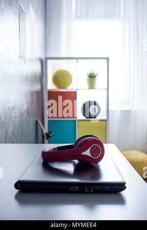 Primo piano della Red Headphones giacente su un laptop con ripiano colorato in background Foto Stock