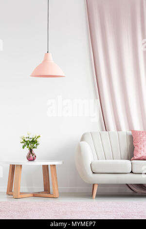 Luminoso soggiorno interno con divano beige, pesca lampada, tavolo in legno e le rose rosa in vaso Foto Stock