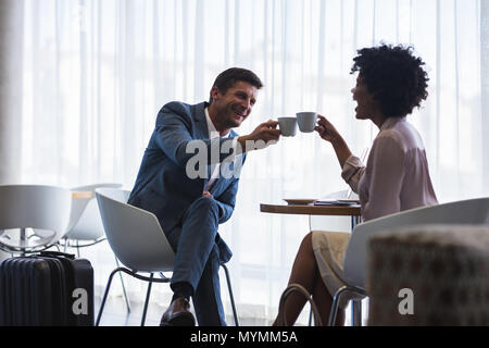 Business Partner seduti all'aeroporto caff fare un brindisi con tazze di caffè. La gente di affari in aeroporto in attesa del loro volo. Foto Stock