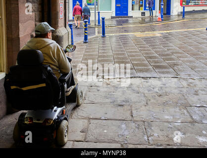 Uomo anziano sulla mobilità scooter si ripara dalla pioggia ad Abergavenny, Waled Foto Stock