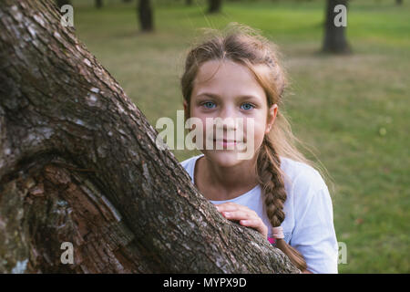 Giocoso bambino bambina che si nasconde dietro la grande tronco di albero da estate Foto Stock