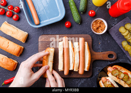 Immagine da sopra dell'uomo facendo hotdog sul bordo di taglio sul tavolo con salsicce Foto Stock