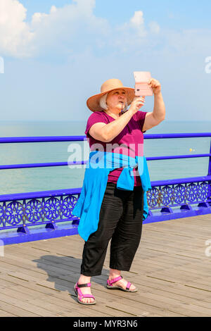 Donna di mezza età tenendo un selfie su Eastbourne Pier Foto Stock