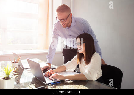 Giovani happy businessman mostrando qualcosa per il suo partner sul computer portatile in ufficio Foto Stock