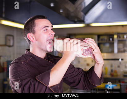 Lo Chef mangiare un Big piese di carne cruda Foto Stock