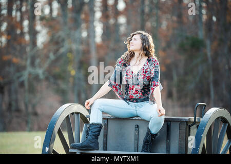 Giovane donna felice seduta manspreading diffondere le gambe sul vecchio carrello cannone in Manassas National Battlefield Park in Virginia dove Bull Run battaglia w Foto Stock