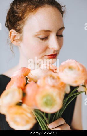 Ritratto di giovane donna con il chiudere gli occhi annusare su un mazzo di fiori di arancio-giallo fiori Foto Stock