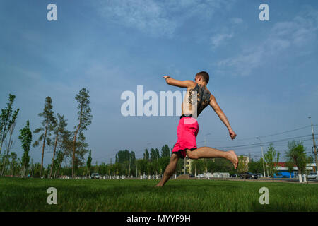 Tricking sul prato nel parco. L uomo è in esecuzione per salto. Arti marziali e parkour. Allenamento di strada. Foto Stock