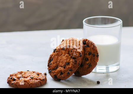 In casa i biscotti al cioccolato e un bicchiere di latte fresco su una pietra bianca dello sfondo. Foto Stock