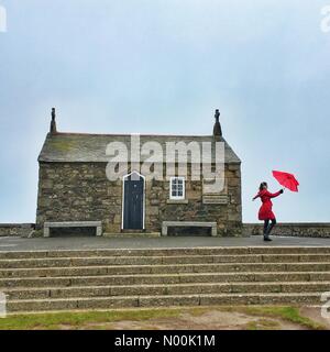 Regno Unito Meteo: giornata di vento per ombrelloni colorati a St Ives. Raich Keene combatte forti raffiche di vento con il suo ombrellone in St Ives costa alla antica cappella di San Nicola. Foto Stock