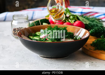 Una sana insalata di verdure fresche a rendere. Donna con le mani in mano versando olio d'oliva in una ciotola con insalata. La cottura di passo dopo passo concetto. Foto Stock