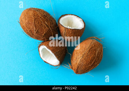 Intero e halfs di noci di cocco su uno sfondo blu. Vista superiore e spazio di copia. Foto Stock