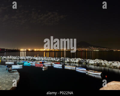 Vista notturna di piccolo molo con barche colorate sulle luci della città e del Monte Vesuvio background in Napoli Foto Stock