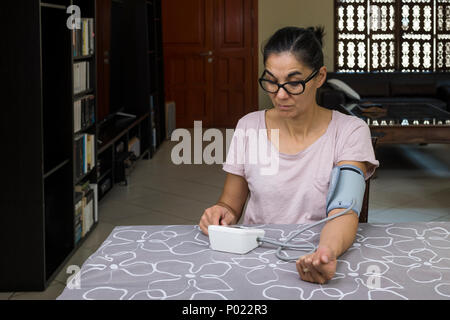 Una donna di 40 anni controlla la pressione sanguigna con un monitor automatico a casa, il monitoraggio della salute personale e l'autoassistenza in un ambiente accogliente Foto Stock