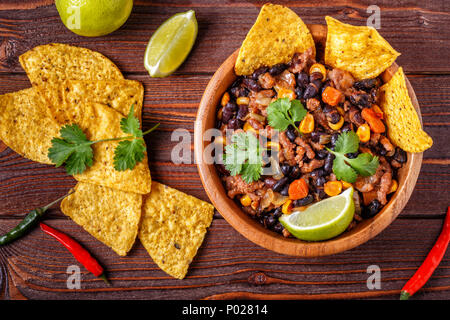 Chili con carne nella ciotola con tortilla chips su sfondo di legno. Foto Stock