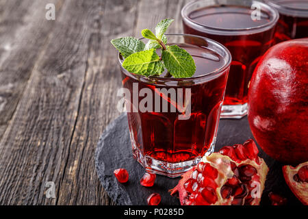 Bicchieri di succo di melograno con freschi frutti di melograno e menta sulla tavola di legno, bibita salutare concetto. Foto Stock