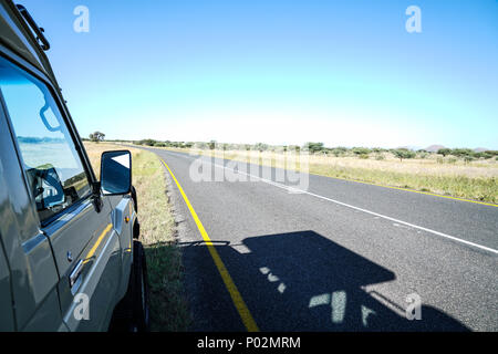 Ombra di safari veicolo parcheggiato sulla strada. Viaggiando attraverso i paesaggi di laminazione e apparentemente non finisce mai di strade della Namibia Foto Stock