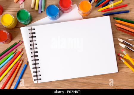Schermata bianca vuota art book su un banco di scuola con vari colori, matite colorate e matite. Foto Stock