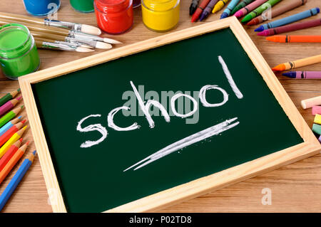 La scuola di parola scritta su una piccola lavagna elementari con vari colori, matite colorate e matite su un banco di scuola. Foto Stock
