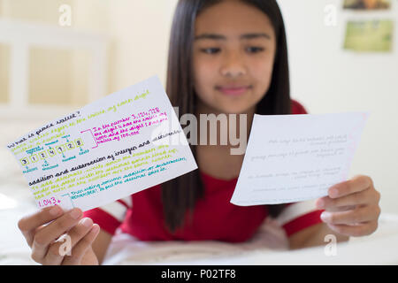 Ragazza distesa sul letto scritto utilizzando le schede di studio per aiutare con la revisione Foto Stock