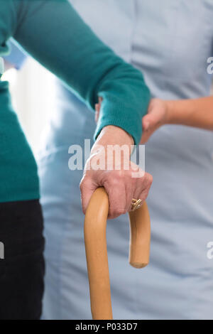 Senior Womans mani sul bastone con cura lavoratore in background Foto Stock