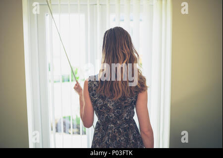 Una giovane donna è aprire le tende a casa Foto Stock