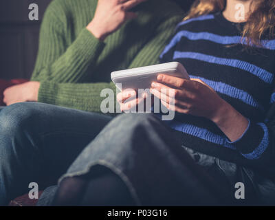 Due giovani genitori seduto su un divano sono in cerca di un baby monitor Foto Stock